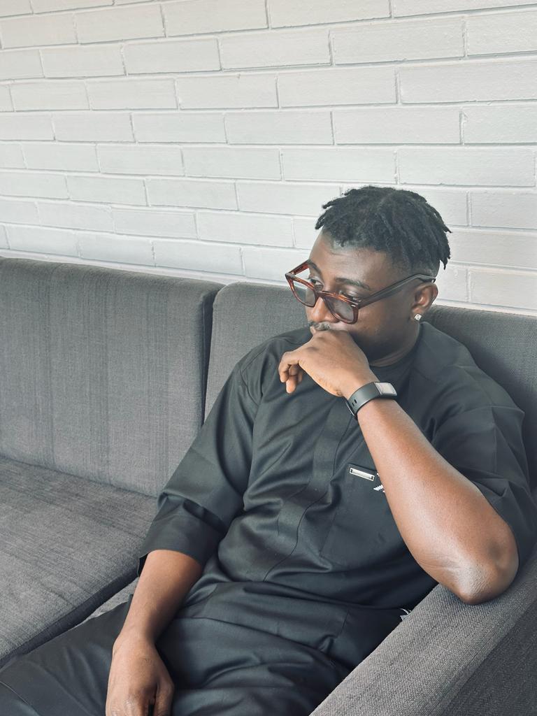 Desmond seated on a sofa in front of a white brick wall