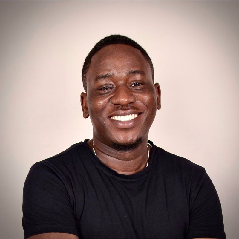 Smiling man with short hair wearing a black t-shirt against a neutral background.